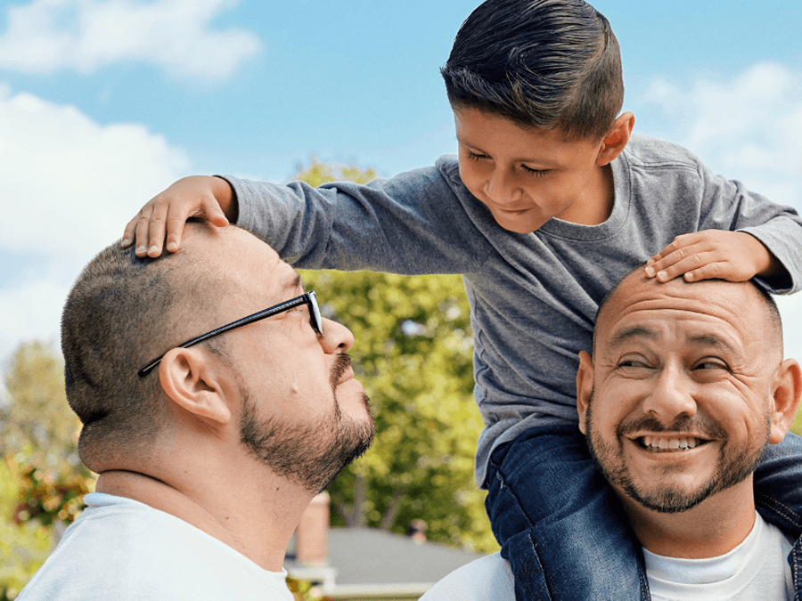 Two dads with a young child on one of their shoulders