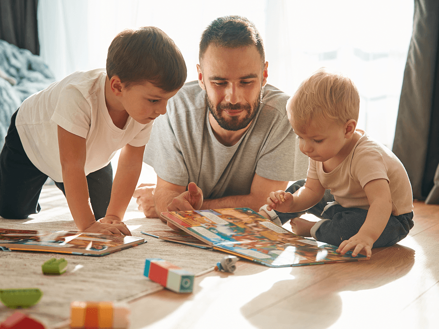 Dad reading and playing with young kids on the floor