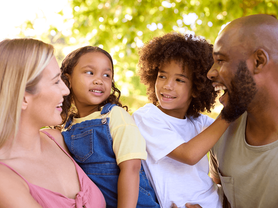 Multiracial family with two kids smiling at each other outside